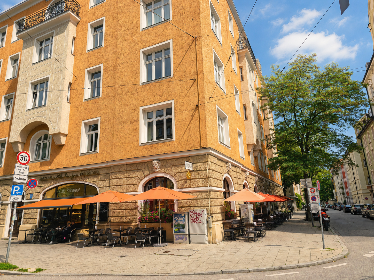Das Eckhaus in der Wörthstraße mit den orangen Schirmen. Unter dem Schriftzug des Cafés steht links der der Bäckerei-Konditorei im selben Haus.